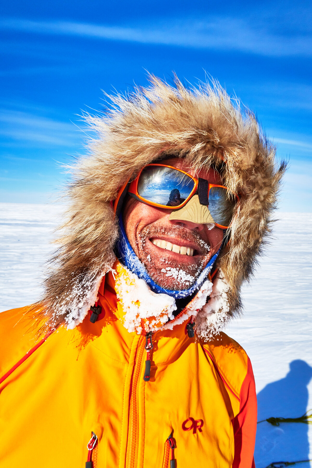 Skier smiles wearing fur ruff, sunglasses, and nose shield